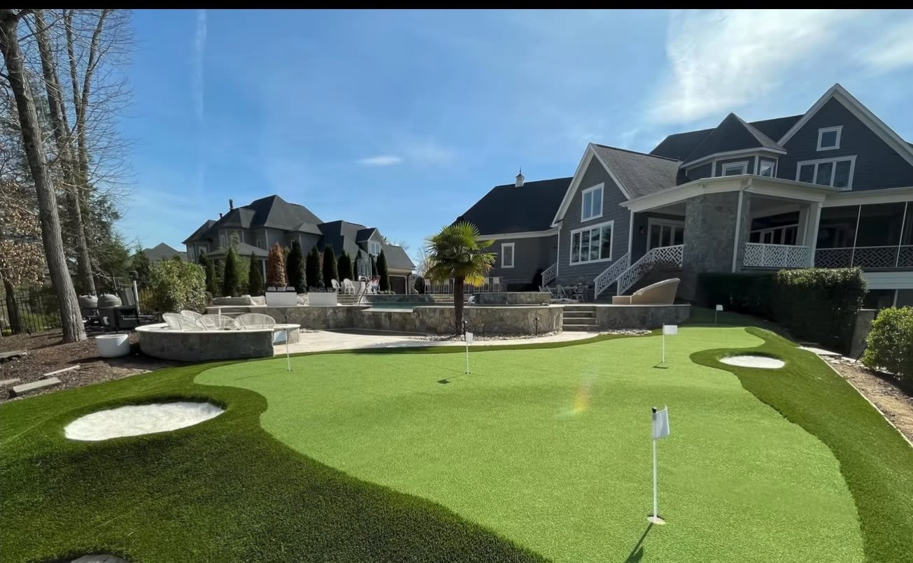 Backyard putting green with sand bunkers below a large lakefront home