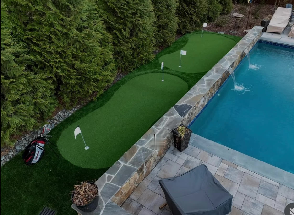 Poolside putting green with three cups beside a stone-capped pool wall