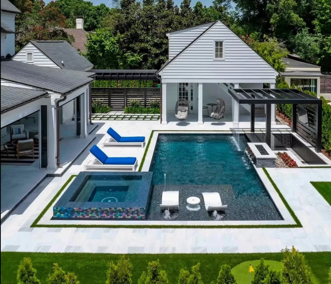Pool and spa framed by turf strips beside a white pool house